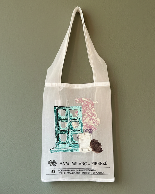 A cream-colored reusable organza fabric tote bag with printed artwork of a teal window, pink cherry tree and a signature V.VM Home Candle. 